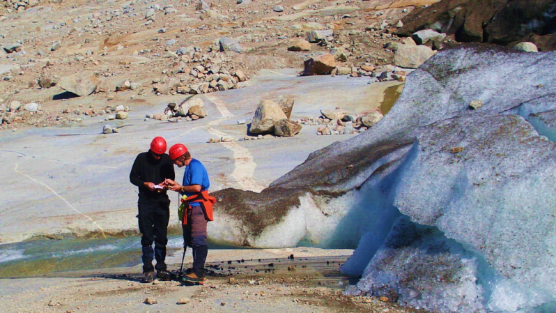 two people next to a glacier looking a notbook