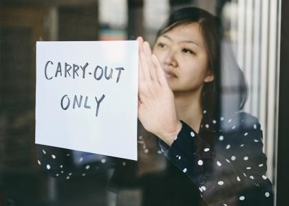 Woman hanging "carry-out online" sign in restaurant window