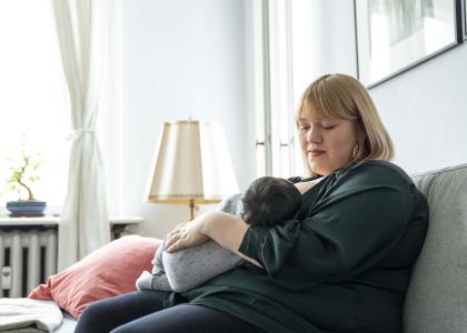 Woman sits on a couch breastfeeding a baby