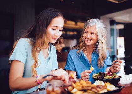 older woman smiles at her adult daughter while they eat at a restaurant together