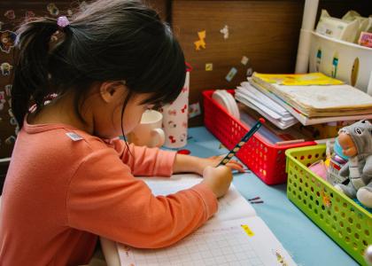 Young girl with black pony tail and orange shirt completing worksheet