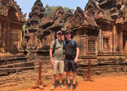 two men standing in front of statues in Angkor Wat, Cambodia