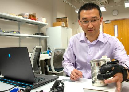 A person wearing a glove-like device lifts a can. 