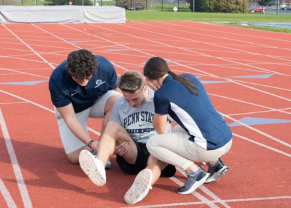 Two athletic training students work with a student athlete who has hurt themselves and needs medical attention.