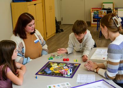 Two speech language pathology students play a therapeutic board game with 2 children