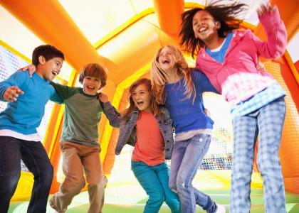 Preteens children of various races, sexes, and ages jumping in a brightly colored bounce house