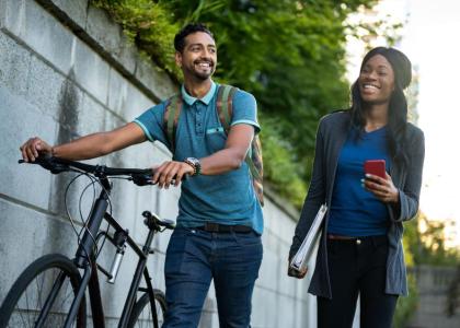 Young man pushing bike walking next two young woman carrying a binder and a smartphone