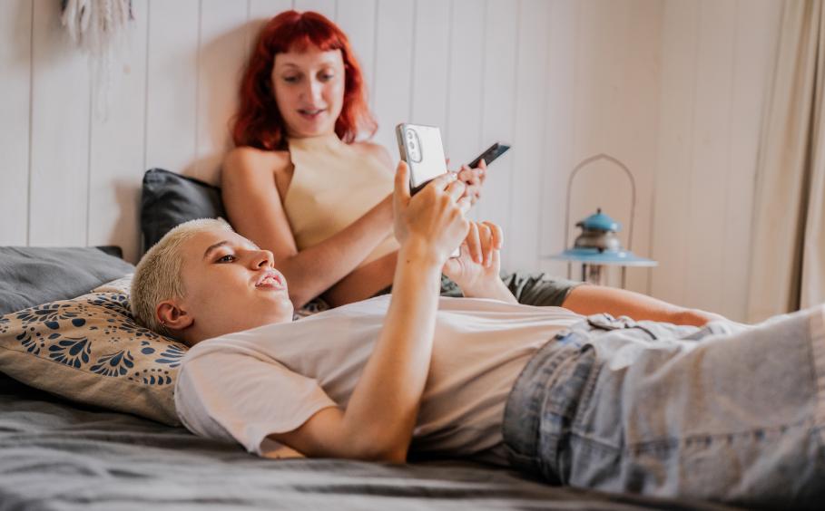 Two young people laying on a bed on their cell phones