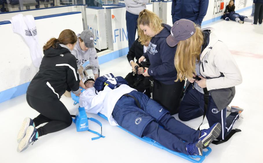 Athletic training students using a training dummy on a hockey rink.