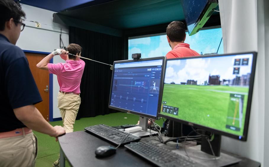 Two computers in the foreground and two instructors working with a golfer in the Golf Teaching and Research Center 