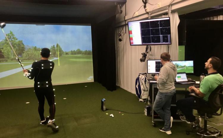 Man in a laboratory wears motion trackers to map his golf swing as researchers look on