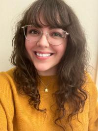 woman with long brown hair and glasses wearing yellow sweater